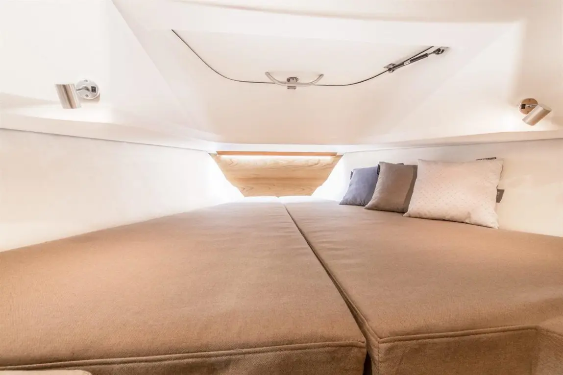 Cozy boat interior featuring a large beige bed with two decorative cushions and a porthole allowing natural light.